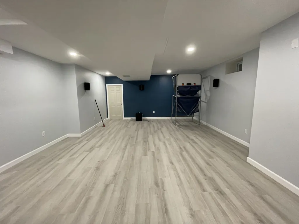 Finished basement with a navy accent wall, light plank flooring and recessed lighting