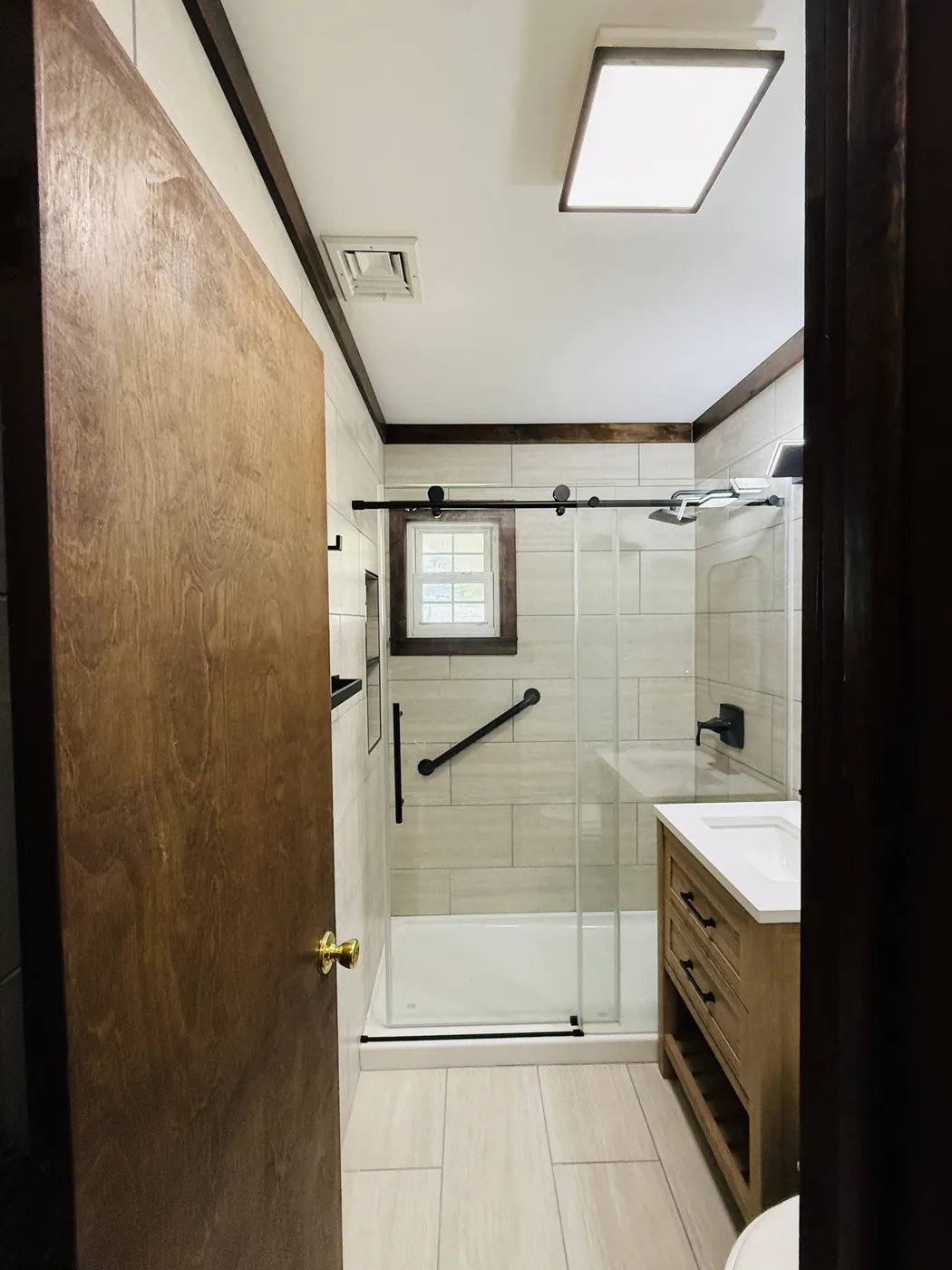 Remodelled bathroom with a large tile shower, sliding glass door, black fixtures and a wood vanity